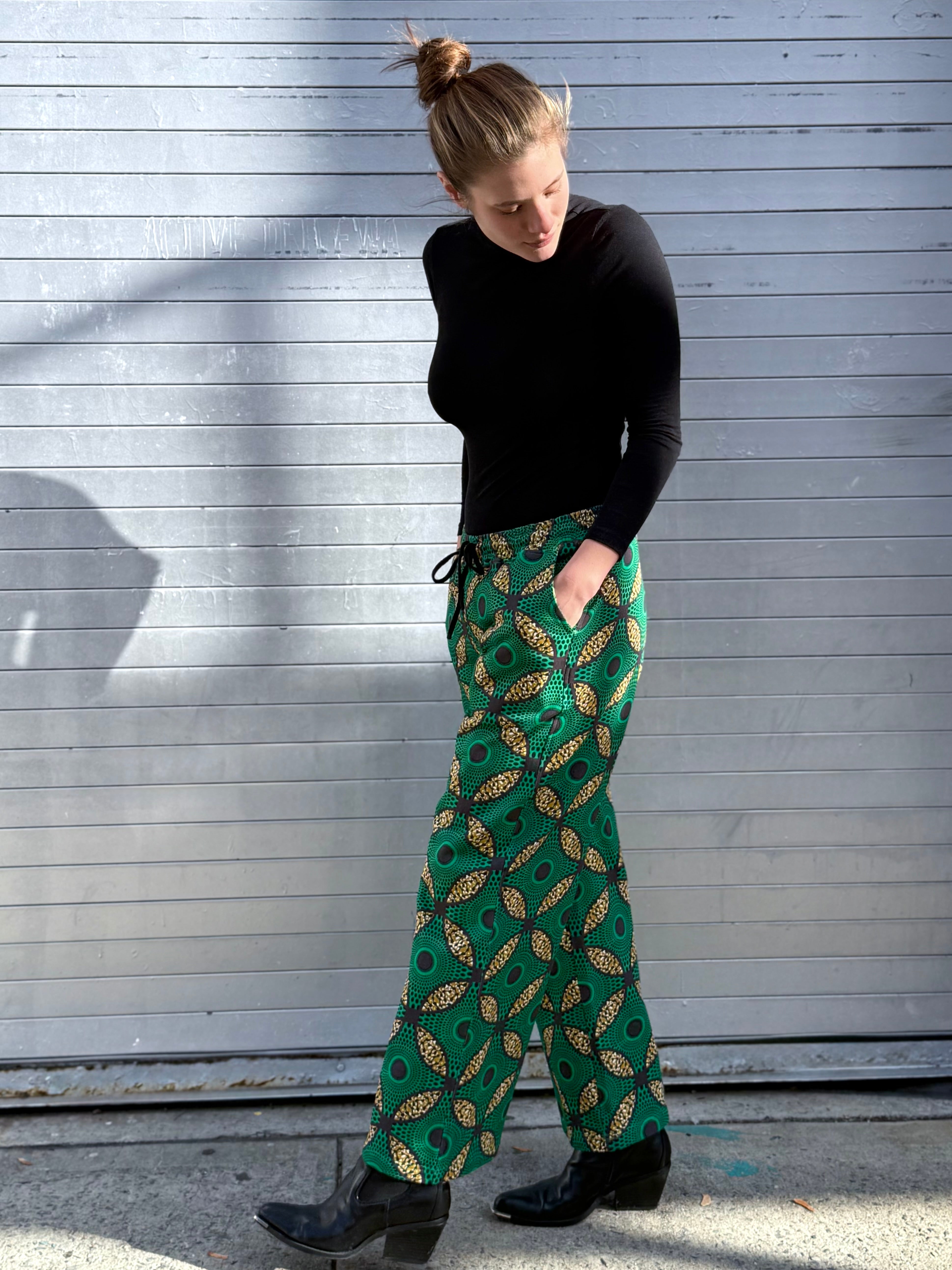 Model wearing the Ìmọ̀lẹ̀ Green Sweat Pants by Lola Faturoti Loves, featuring a vibrant Yoruba-inspired pattern in green, gold, and black. Ethically made from organic cotton with eco-friendly inks, these pants embody conscious design and effortless elegance.