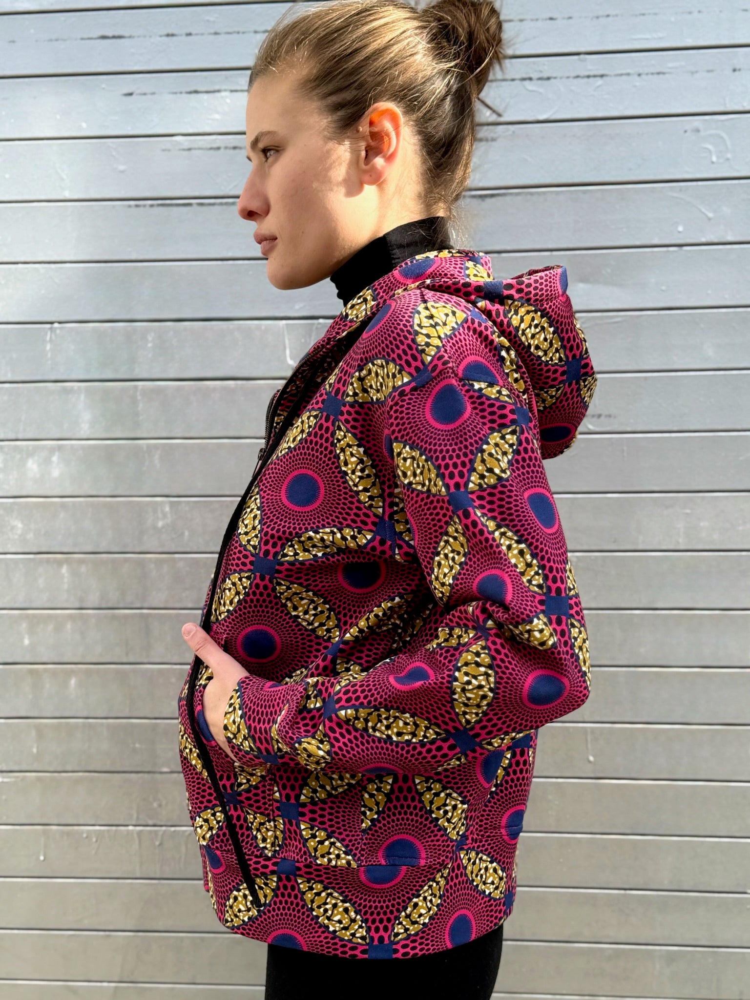 Side view of model wearing the Ìmọ́lẹ̀ Pink Hoodie by Lola Faturoti Loves, showing the bold Yoruba geometric pattern in pink and yellow. Ethically produced in India from organic cotton, this sustainable hoodie represents empowerment, culture, and everyday comfort.