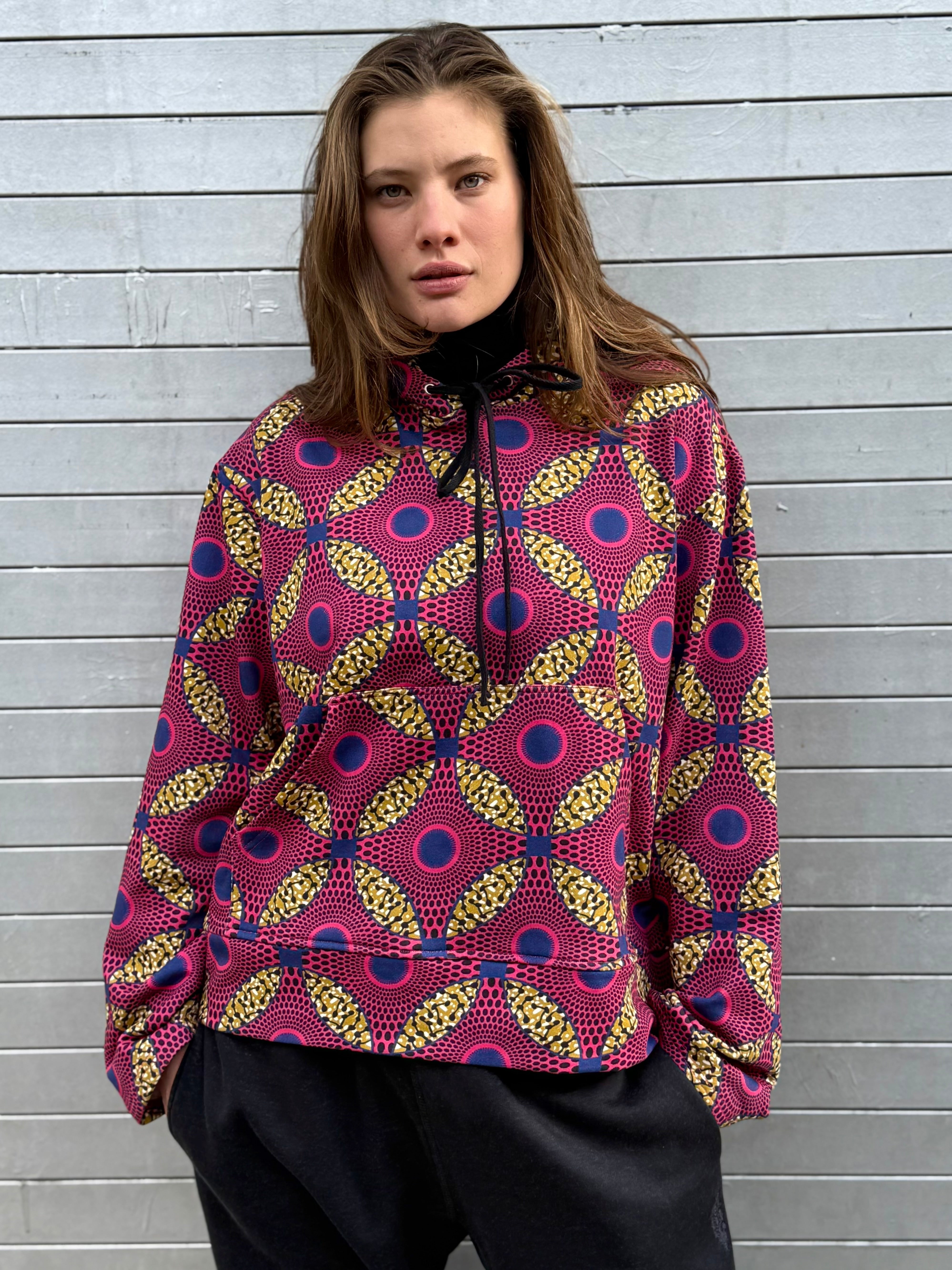 Model wearing the Ìmọ́lẹ̀ Pink Sweat Hoodie by Lola Faturoti Loves, featuring a bold Yoruba-inspired print in pink, navy, and yellow. Ethically crafted from organic cotton and printed with eco-friendly inks, this limited-edition hoodie brings vibrancy, empowerment, and warmth to winter days.