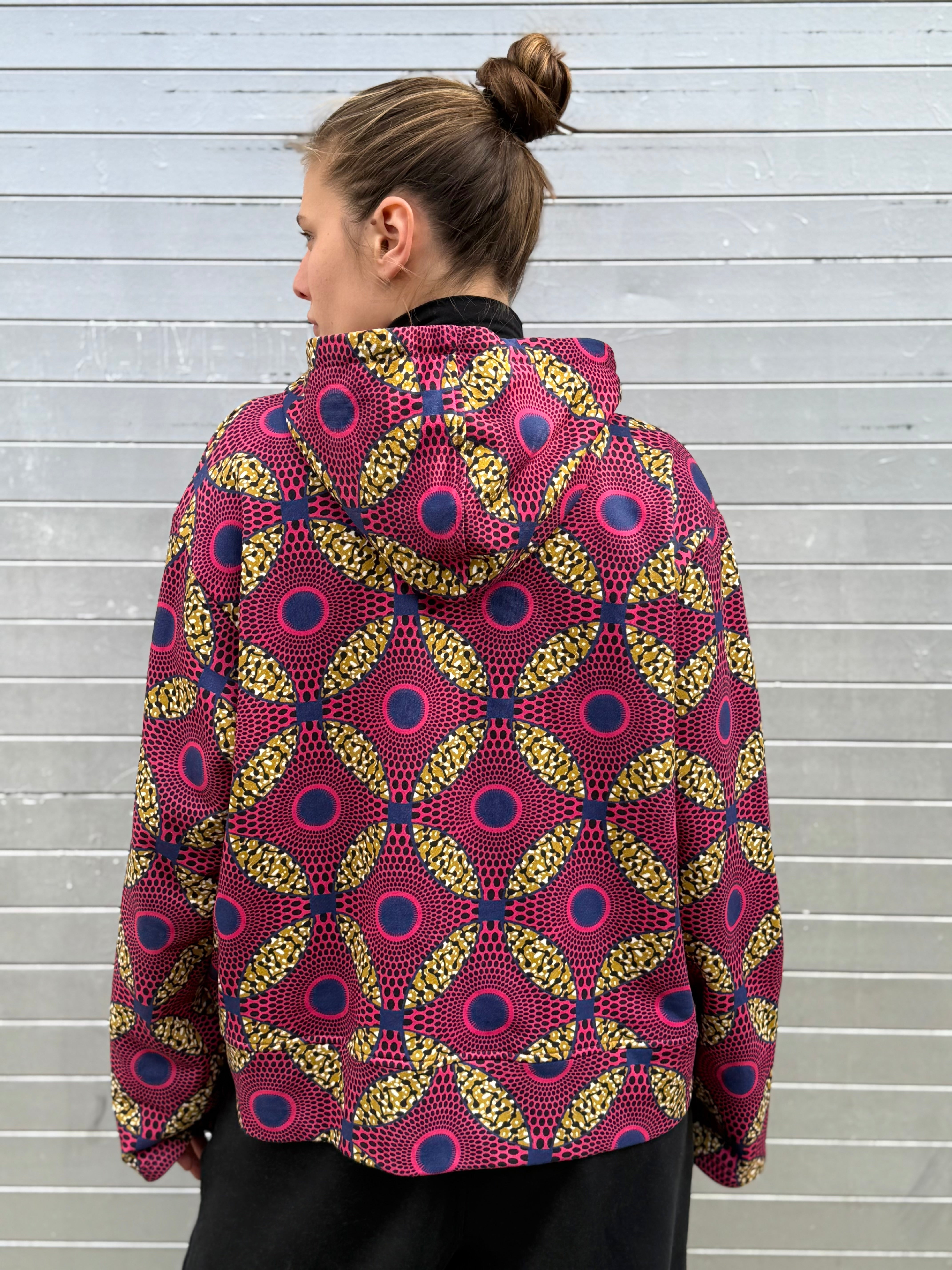 Back view of the Ìmọ́lẹ̀ Pink Sweat Hoodie by Lola Faturoti Loves, showcasing the Yoruba-inspired circular print in deep pink, navy blue, and yellow. Ethically made from organic cotton and printed with eco-friendly inks, it embodies warmth, empowerment, and creative energy.
