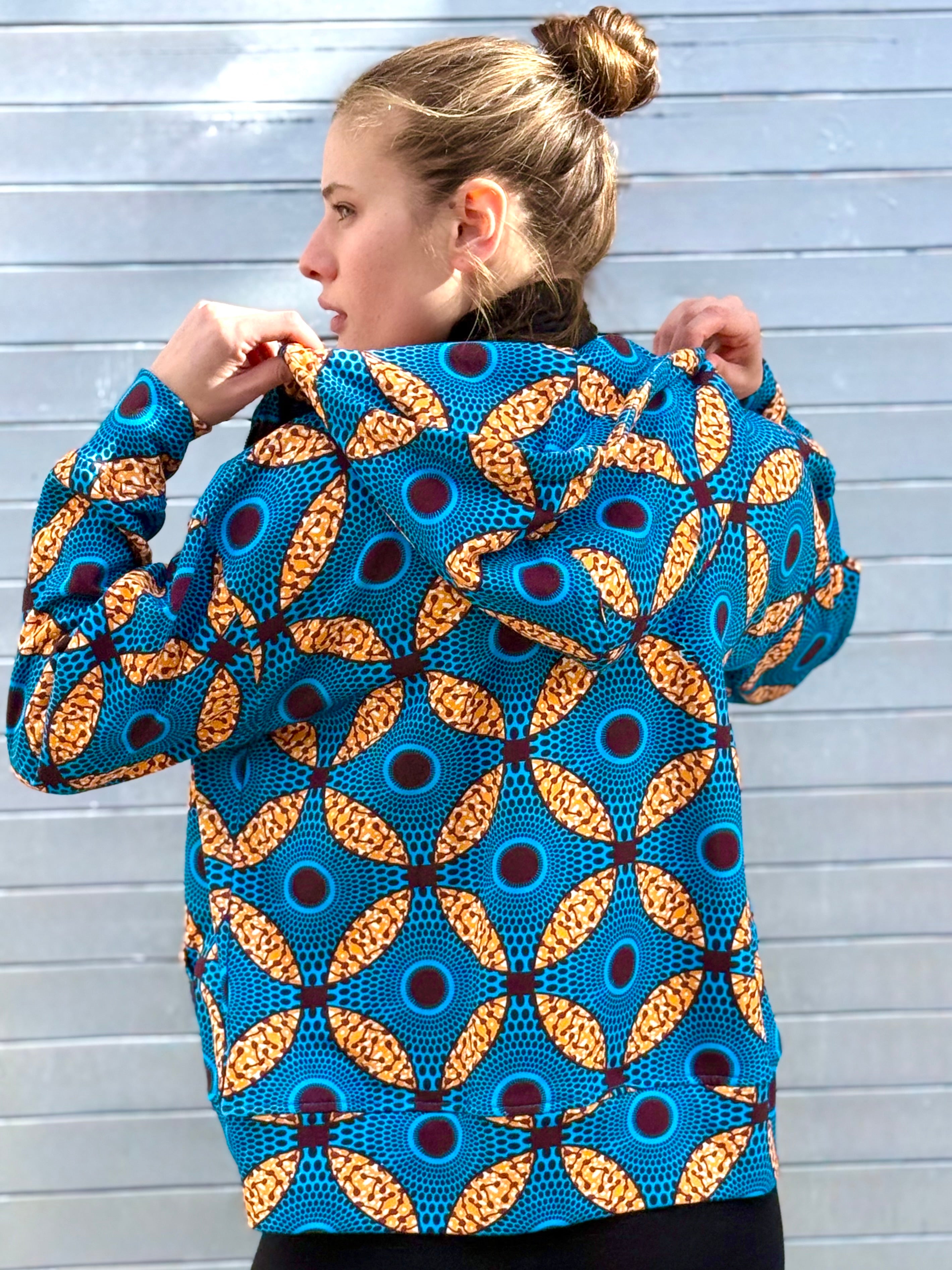Model turning slightly to reveal the hood and back of the Ìmọ́lẹ̀ Blue Hoodie, featuring signature Yoruba-inspired prints. Designed by Lola Faturoti Loves, it represents sustainable craftsmanship and the fusion of African heritage with contemporary design.