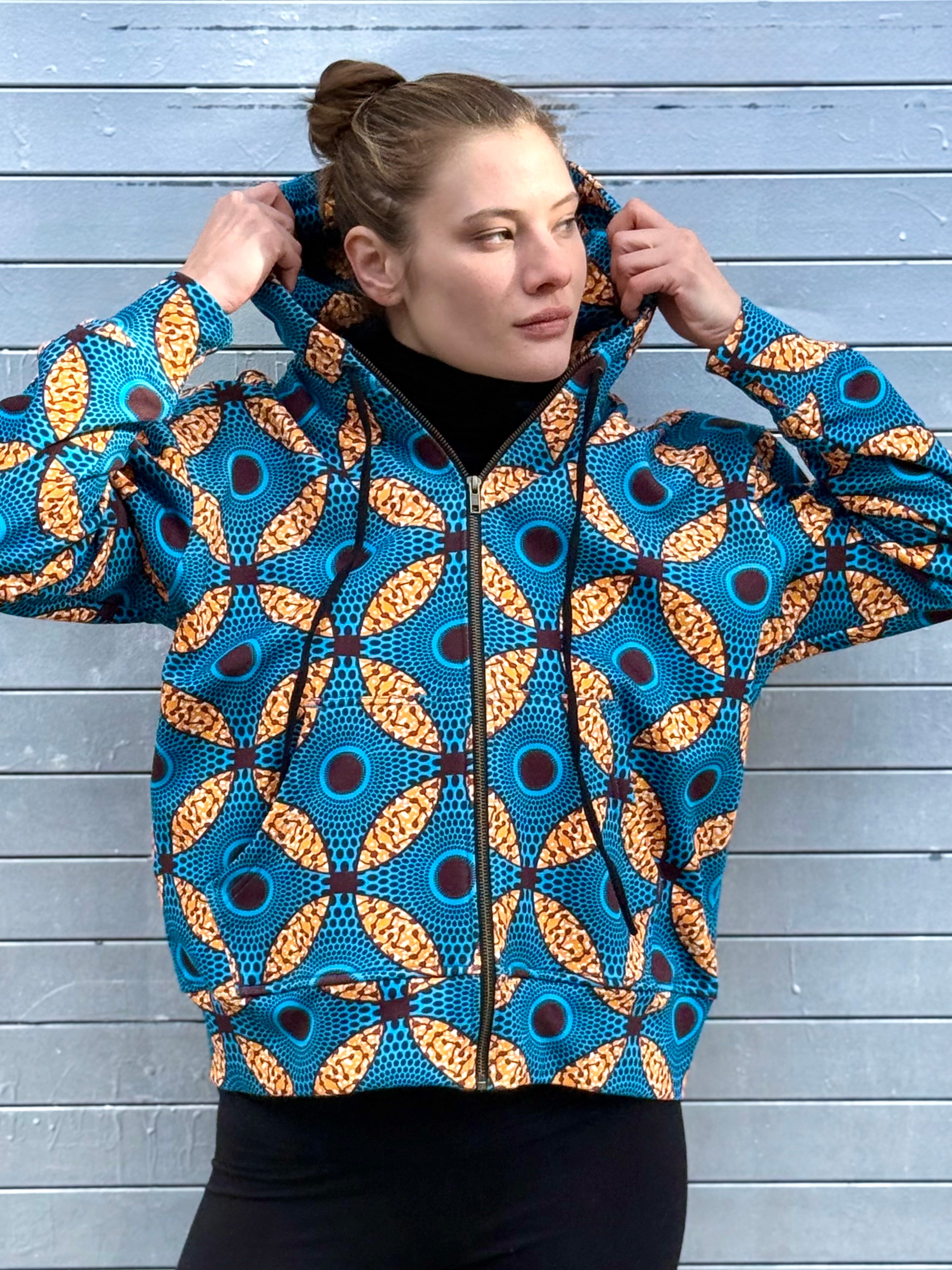 Model adjusting the hood of the Ìmọ́lẹ̀ Blue Hoodie, revealing the detailed Yoruba geometric print. Crafted in organic cotton with eco-friendly inks, this sustainable zip-up by Lola Faturoti Loves merges artistry, culture, and comfort.
