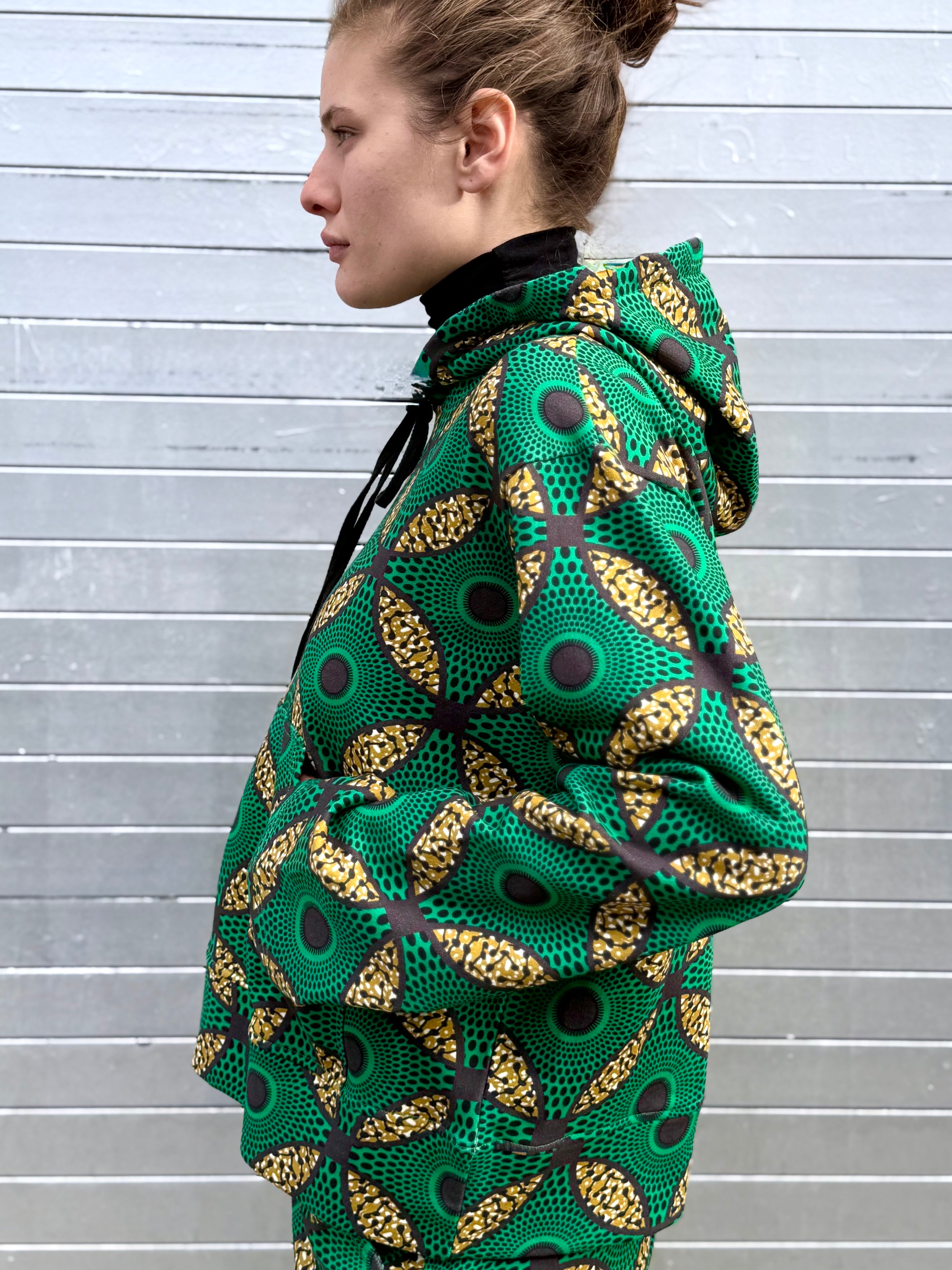 Model in profile wearing the Ìmọ́lẹ̀ Green Sweat Hoodie by Lola Faturoti Loves. The bright green and gold Yoruba-inspired design evokes energy, resilience, and conscious craftsmanship.
