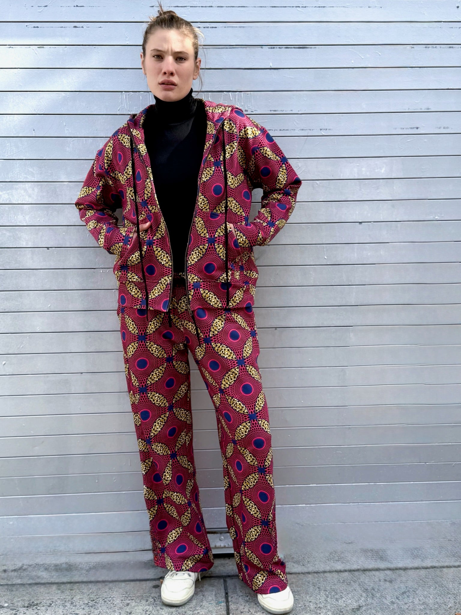 Full-body image of the Ìmọ́lẹ̀ Pink Hoodie by Lola Faturoti Loves, styled with black pants and ankle boots. Crafted from organic cotton and printed sustainably, this hoodie merges cultural vibrancy, urban minimalism, and modern femininity.