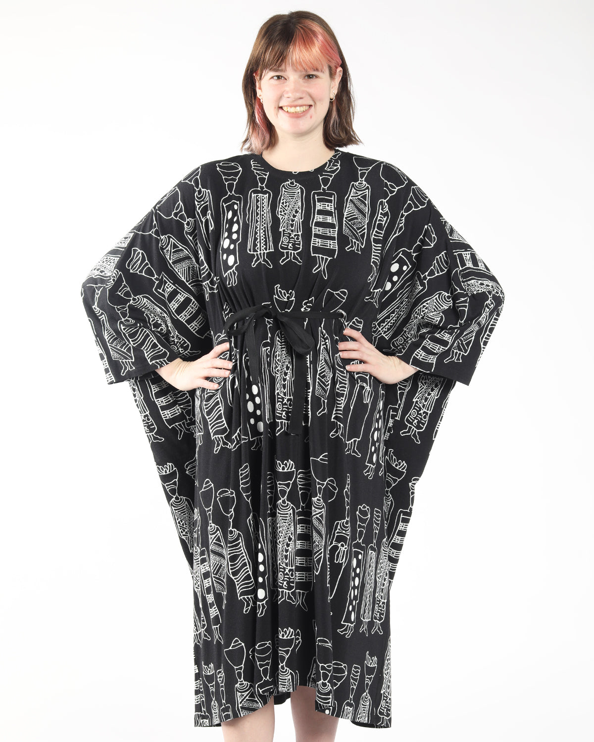 model wearing a black oversize bamboo dress in symbolic african print, and a front tie belt for adjustable waist cinching