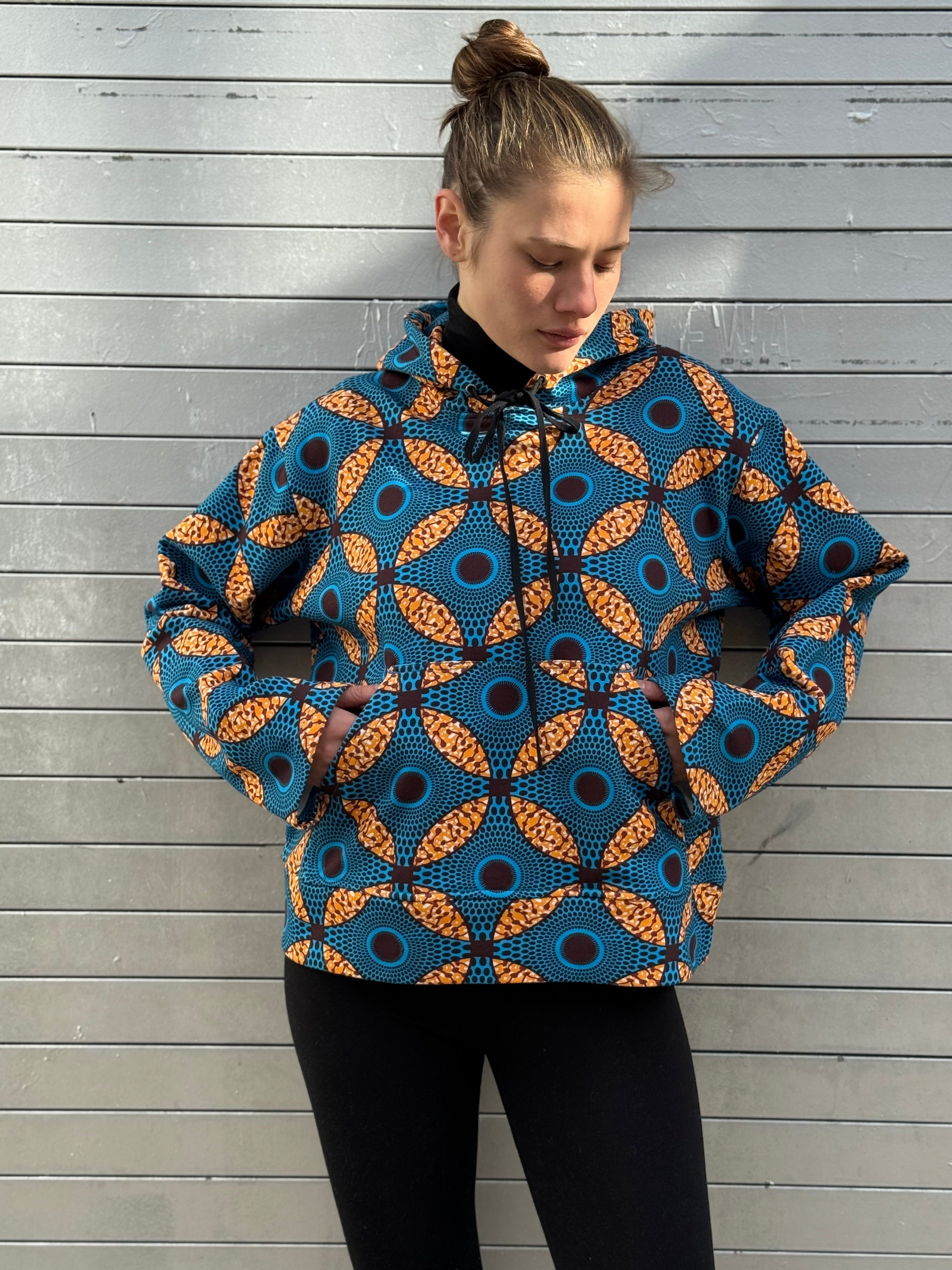 Close-up of the Ìmọ́lẹ̀ Blue Hoodie’s pattern, showing the intricate Yoruba-inspired design in cobalt and amber tones. Ethically made from organic cotton, it offers comfort, vibrancy, and a reminder of connection through culture.