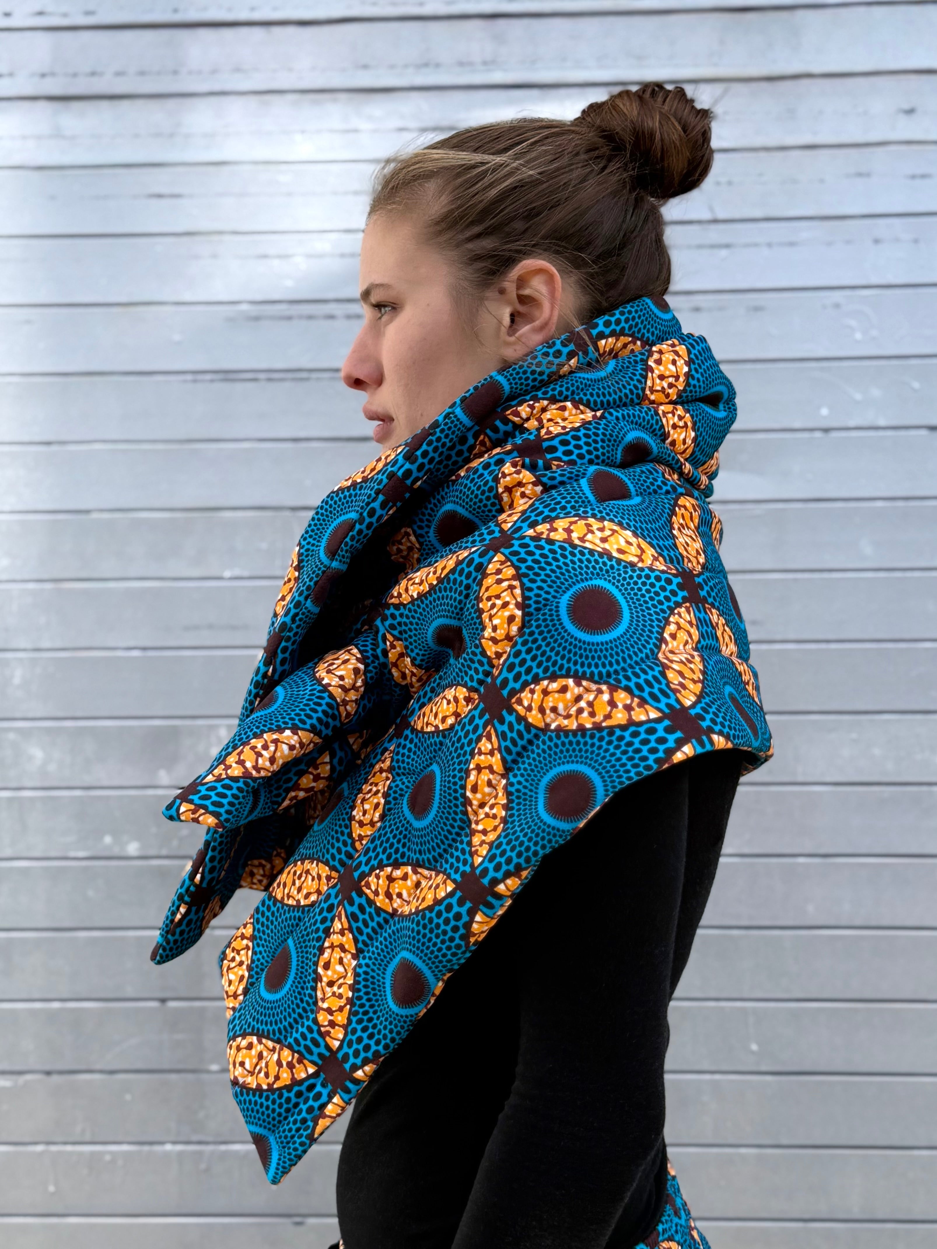 Side profile of model wearing a blue padded quilted scarf with African-inspired print from the Ìmọ́lẹ̀ Sweat Capsule by Lola Faturoti Loves. Elegant side view of the Ìmọ́lẹ̀ scarf in blue: a fair-trade quilted wrap merging heritage craft and modern comfort.