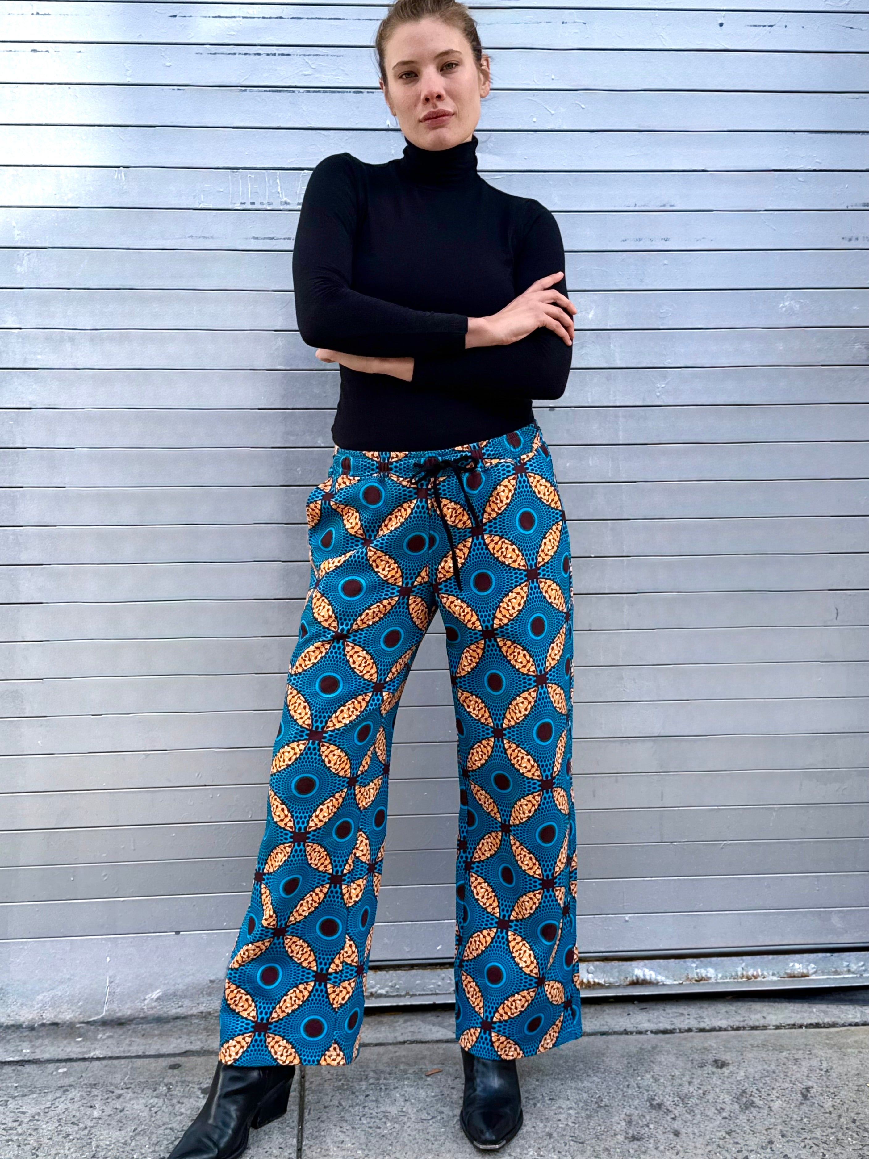 Model wearing the Ìmọ̀lẹ̀ Blue Sweat Pants by Lola Faturoti Loves, featuring a vibrant Yoruba-inspired print in blue, yellow, and black. Made from soft organic cotton with eco-friendly inks, these pants combine bold artistry with everyday ease and movement.