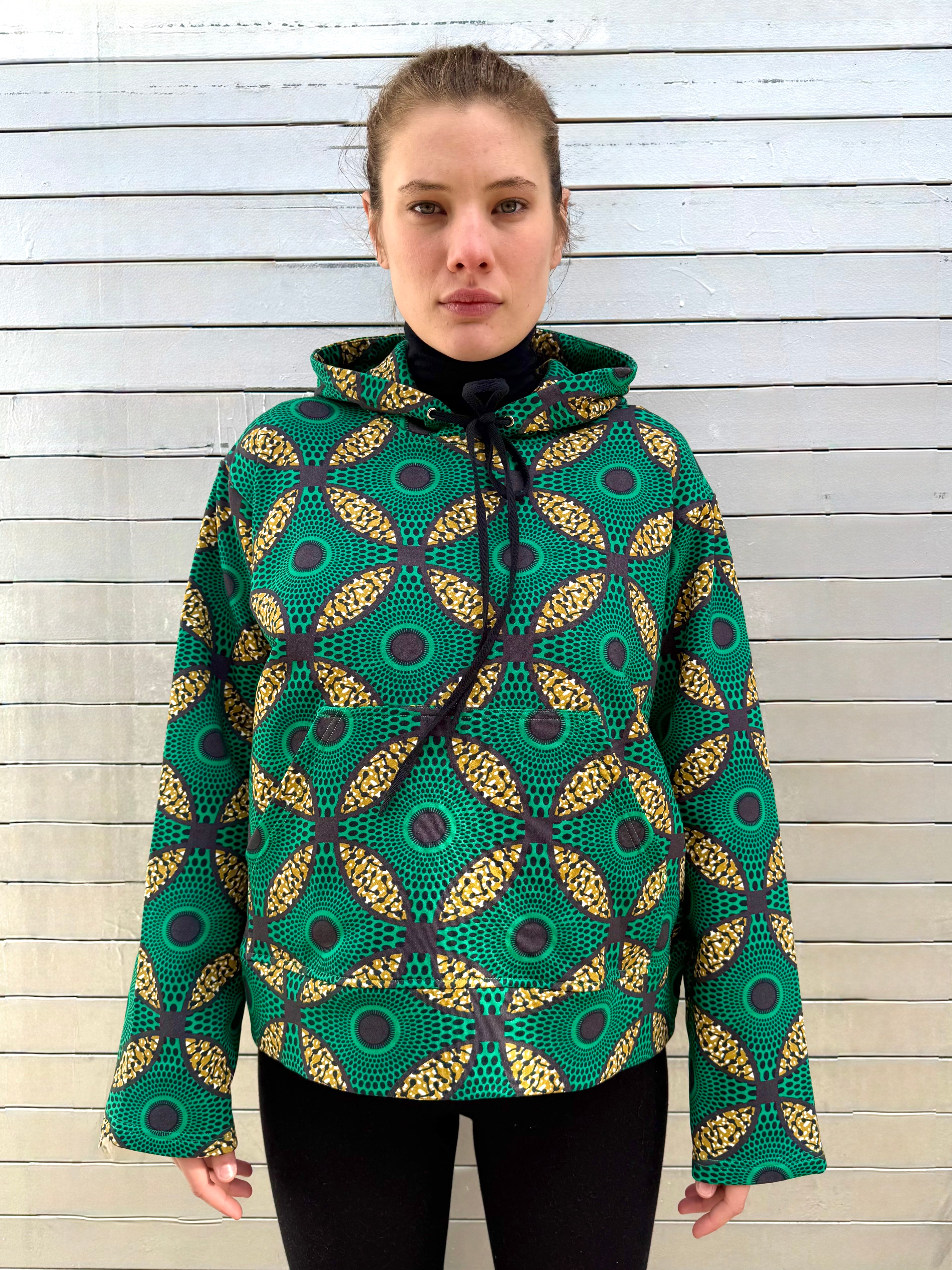 Model wearing the Ìmọ́lẹ̀ Green Sweat Hoodie by Lola Faturoti Loves, featuring a bold Yoruba-inspired print in emerald green and golden amber. Crafted from organic cotton and printed with eco-friendly inks, this hoodie embodies balance, brightness, and sustainable design.